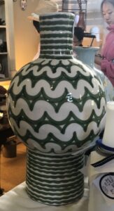 A large, modern white vase with stripes and wavy lines in green