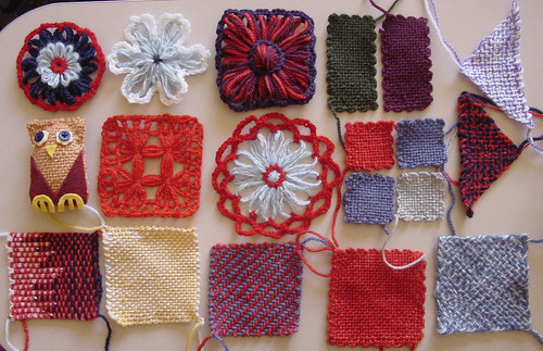 A collection of yarn flowers, pin loom woven shapes, and a small stuffed owl.