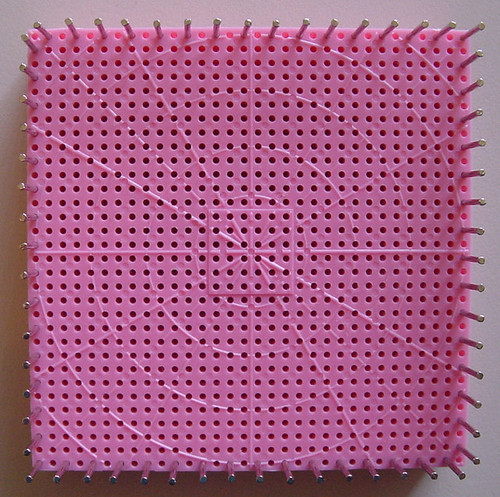 Square pink pin loom with small nailes in every second hole around the outer border.