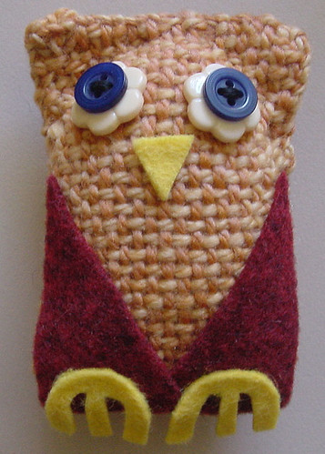 A small owl made from woven arch shapes, with felt feet, wings and beak, and buttons for eyes.