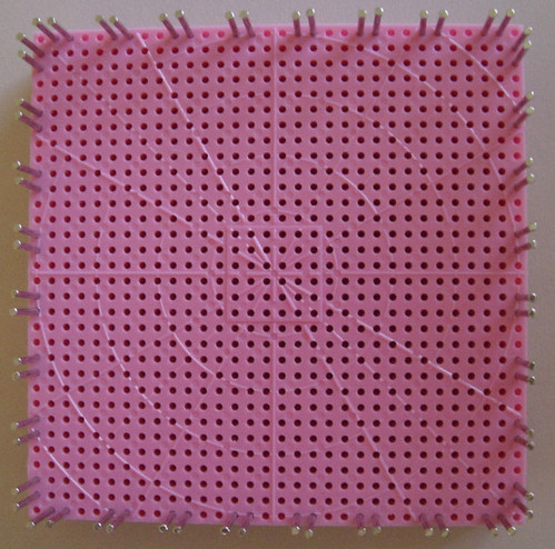 Loom set up with pins around the outer edges. there are two adjacent pins, followed by two empty holes, repeated all around.