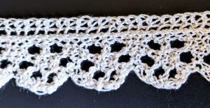 Narrow knitted lace with a scalloped edge and design made of rings of six large eyelets within each scallop.