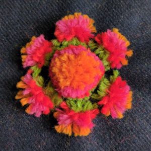 The template has been removed from the fluffy flower and the threads have been roughly brushed into place, filling in the centre to make a larger pompom.