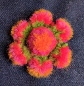 A fuzzy, wool flower that looks like a pompon surrounded by 6 smaller pompoms as petals.