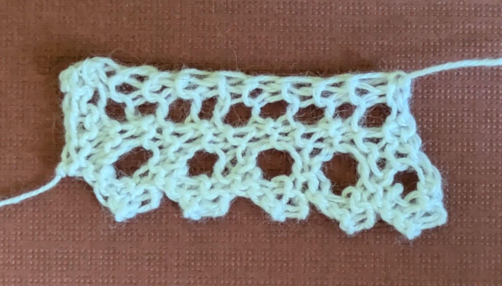 Narrow, knitted lace edging with design of large, single eyelets and a pointed sawtooth edge.