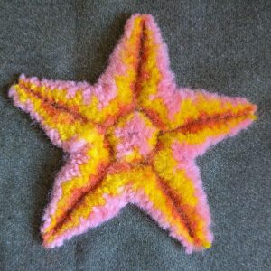 A star shape filled with a fluffy wool pile in layers of orange, yellow and pink.