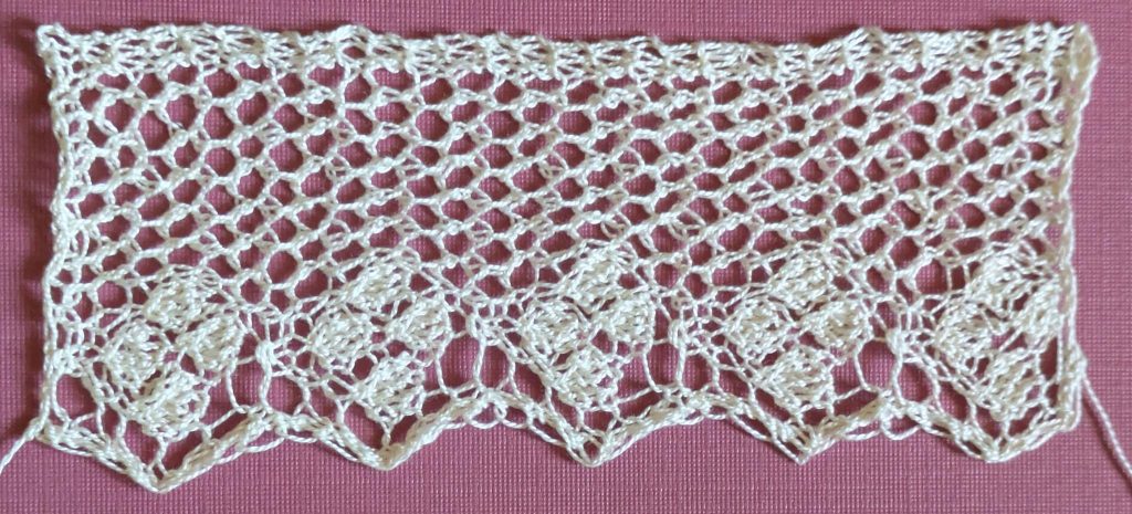 Wide knitted lace with background made of eyelets, and a solid diamond motif in each point made of four single diamonds.