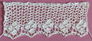 Wide knitted lace with background made of eyelets, and a solid diamond motif in each point made of four single diamonds.